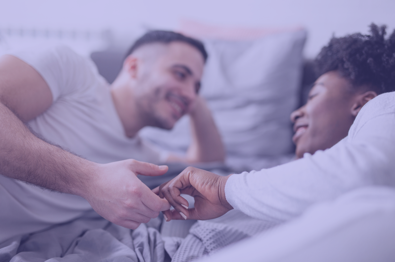 mixed couple in bed smiling and holding hands
